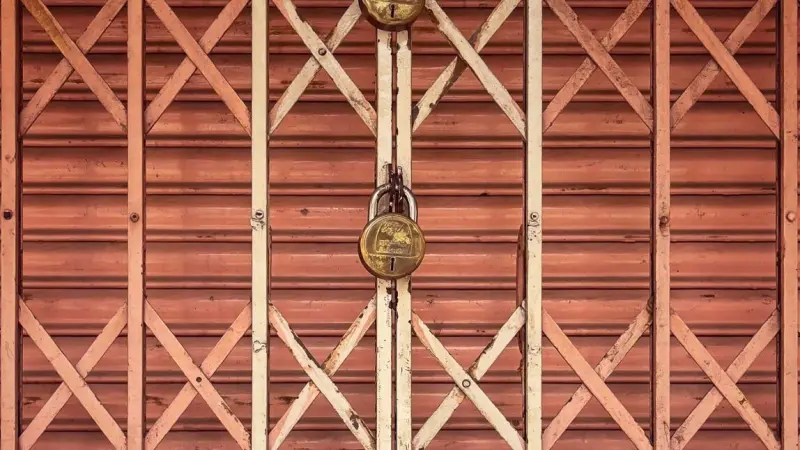 A shuttered shop gate held closed by brass padlocks