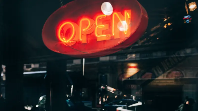 A red neon open sign glowing in a dark storefront window