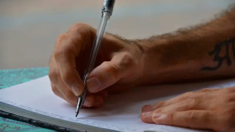 A hand writing notes in an open notebook with a ballpoint pen