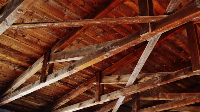 A wooden ceiling seen from below, crossed by rafters and beams