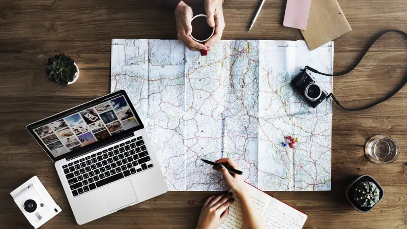 Two people reading a road map on a wooden table, one circling a route with a pen