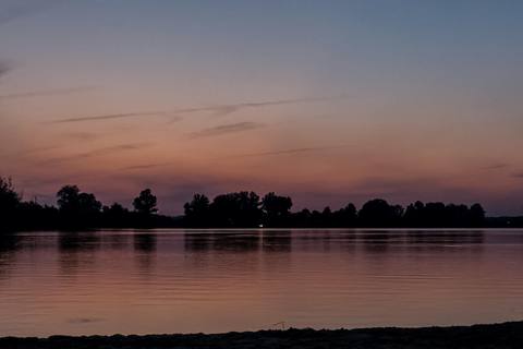 Creve Coeur Lake at sunset, the far shore's trees silhouetted against a fading orange sky.