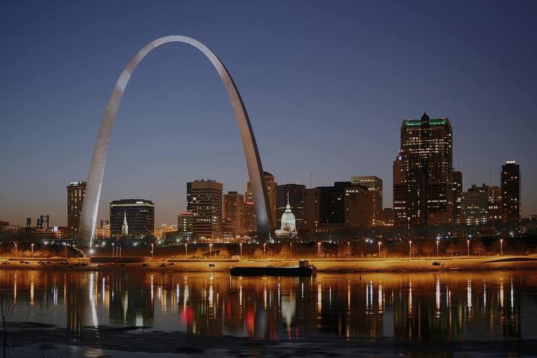 The Gateway Arch and downtown St. Louis skyline at dusk, lights reflecting on the Mississippi River.